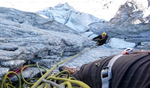 Männlicher Bergsteiger auf Sicherung auf einem harten und exponierten klassischen Aufstieg in den Schweizer Alpen mit einem Gletscher weit unten