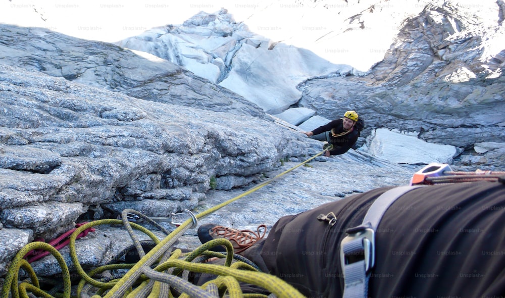 Alpinista in sosta su una classica salita dura ed esposta nelle Alpi svizzere con un ghiacciaio in fondo