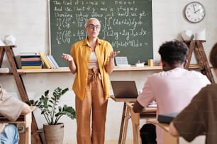 Teacher standing at the blackboard and gesturing she explaining new material to students at university