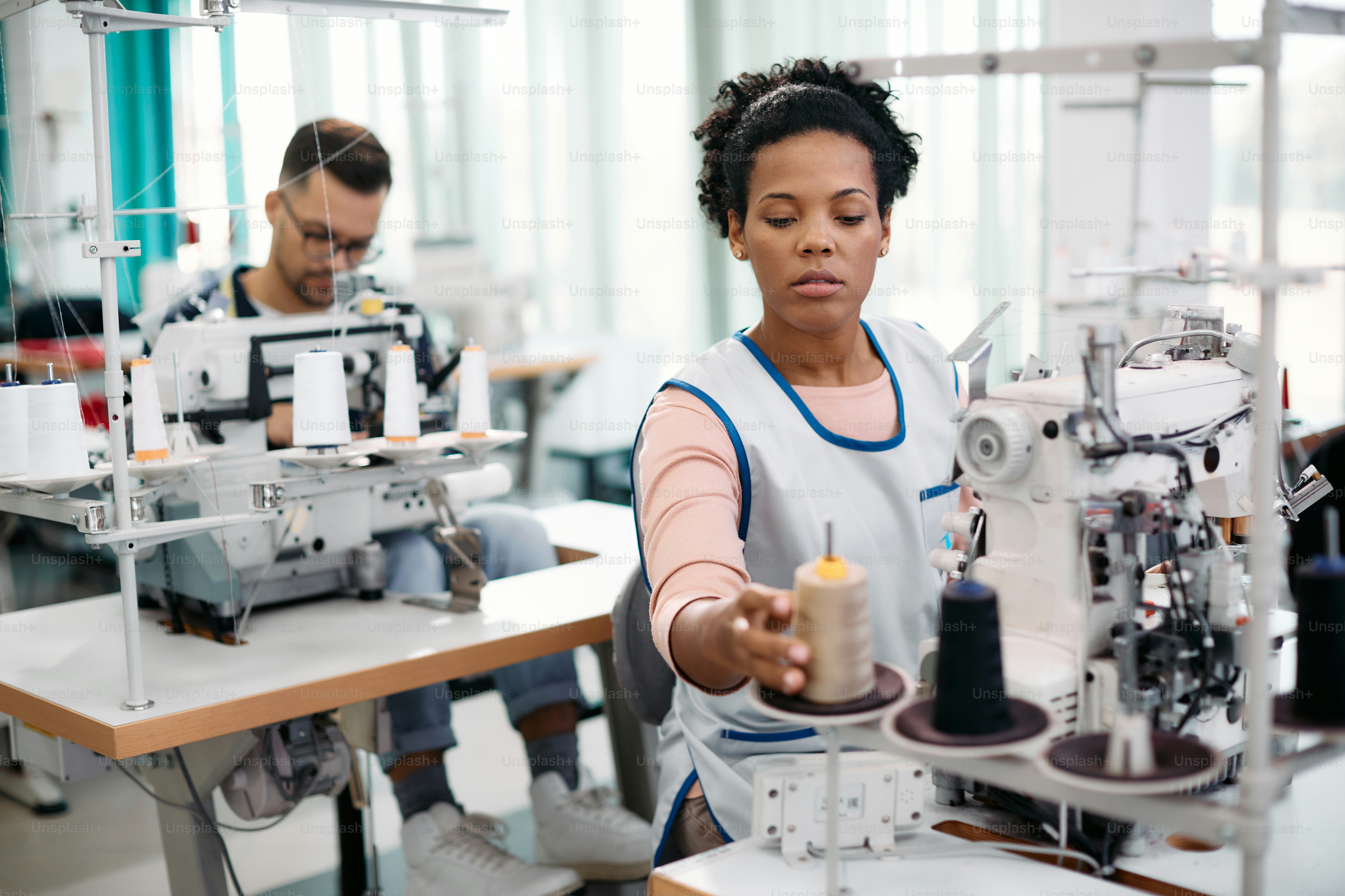 African American dressmaker sets the thread on sewing machine while ...
