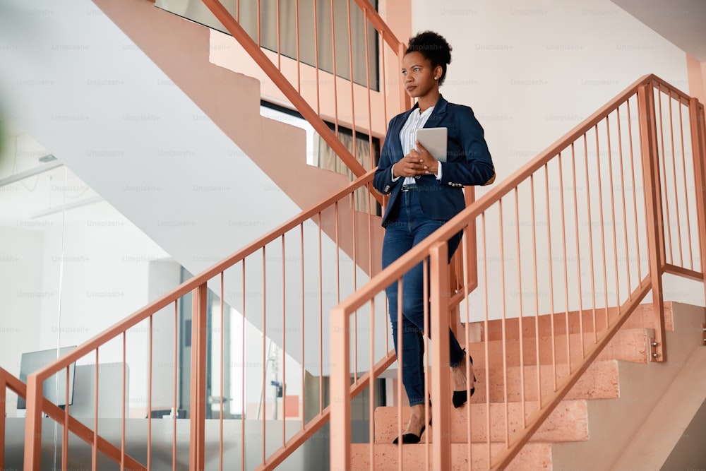 African American businesswoman holding digital tablet while walking down the stairs at work. Copy space.