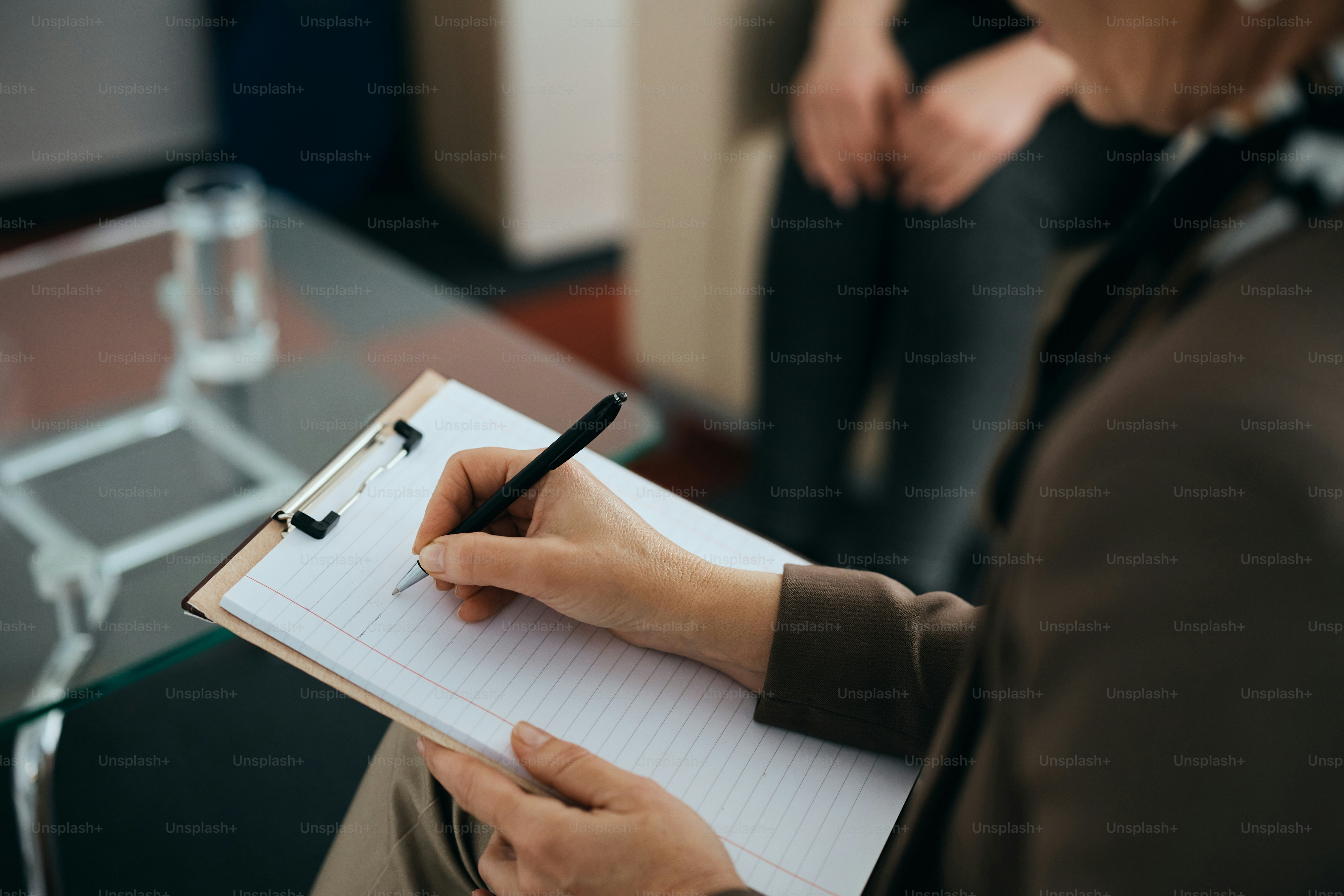Close-up of female psychiatrist writing notes while having therapy session with a patient.