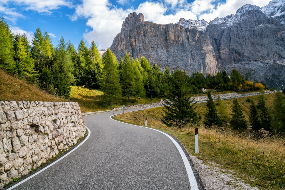 Bella strada di montagna con alberi, boschi e montagne sullo sfondo. Scattata sulla strada statale a Passo Gardena, gruppo montuoso del Sella delle Dolomiti in Italia.