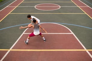 Young sportsman carrying ball while trying to throw it over his rival while playing basketball on court