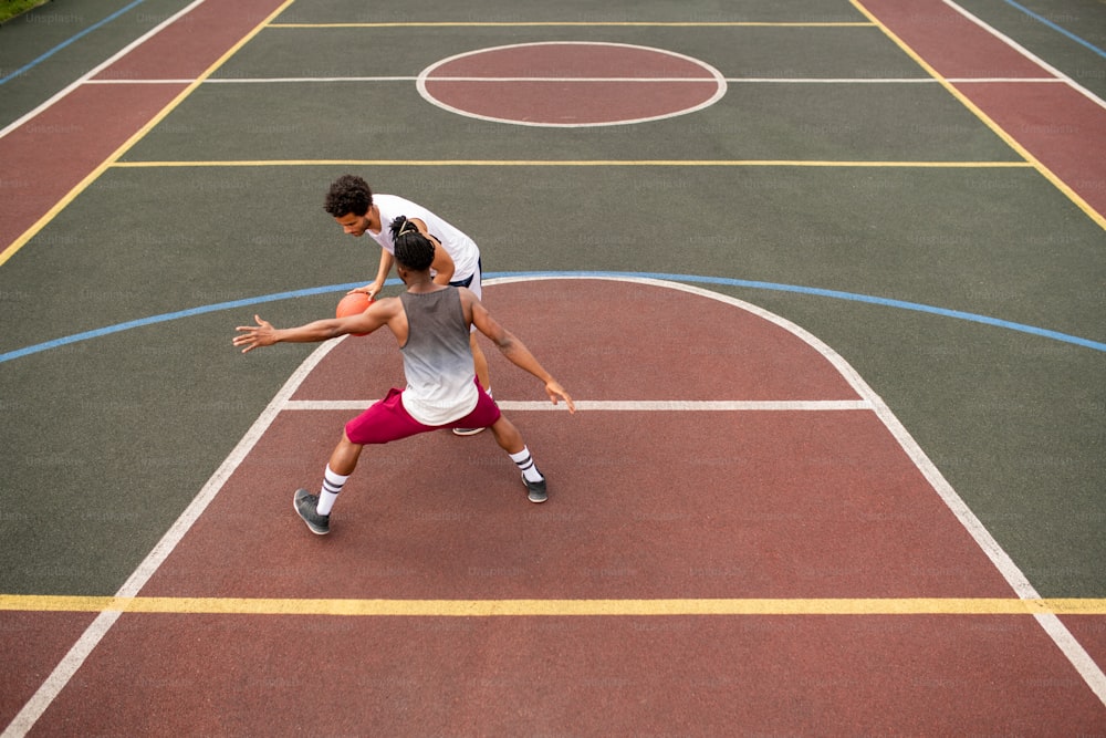 코트에서 농구를 하는 동안 라이벌에게 공을 던지려고 하는 동안 공을 들고 있는 젊은 스포츠맨