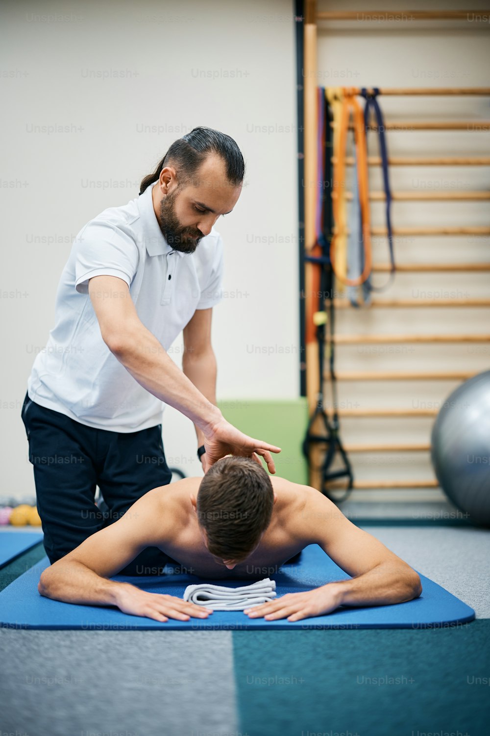 Physical therapist massaging athlete's neck during rehabilitation treatment at health club.