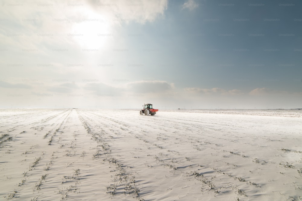 Farmer with tractor seeding - sowing crops at agricultural fields in winter - snow