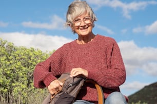 Ritratto di una donna sorridente anziana che riposa in un'escursione all'aperto in campagna guardando la macchina fotografica. Donna matura e attraente in forma durante un'escursione che si gode la libertà dell'avventura e una vacanza sana