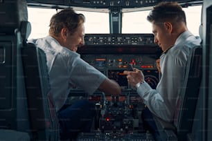 Rückansicht eines Airline-Kapitäns und eines Ersten Offiziers mit Smartphone in der Hand im Cockpit