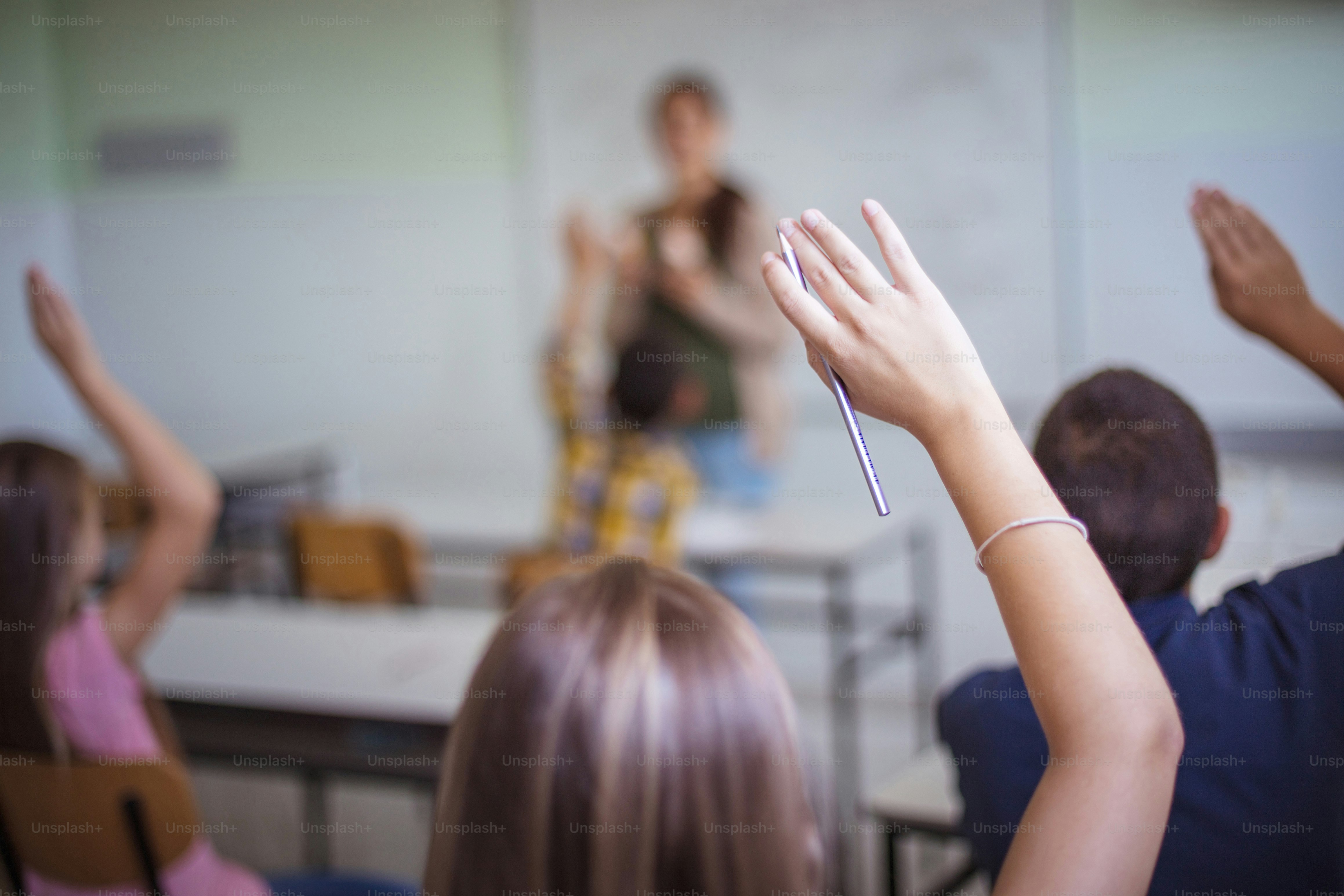 Grupo médio de estudantes levantando os braços para responder à pergunta. Vista traseira de alunos do ensino fundamental levantando os braços em uma classe.