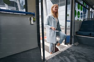Viaggiatore felice sorridente con valigia trolley e biglietto d'imbarco che sale sul bus navetta dell'aeroporto