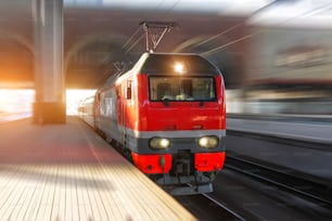 The lead electric locomotive with a passenger train passes at high speed through the city platform at the station