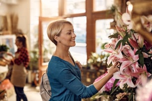 꽃 가게에서 사는 동안 꽃을 보고 있는 행복한 중년 여성.