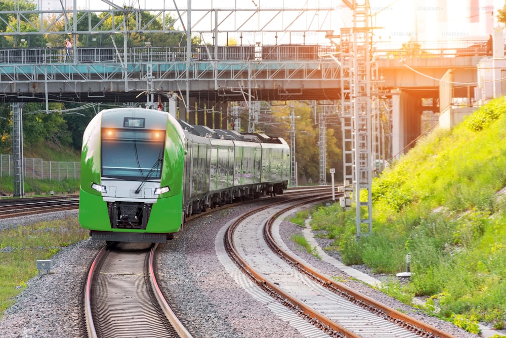 Passenger electric train rides on the turn of the railway line under the automobile bridge