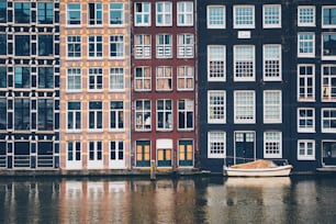 Rangée de maisons typiques et bateau sur le canal d’Amsterdam Damrak avec reflet. Amsterdam, Pays-Bas