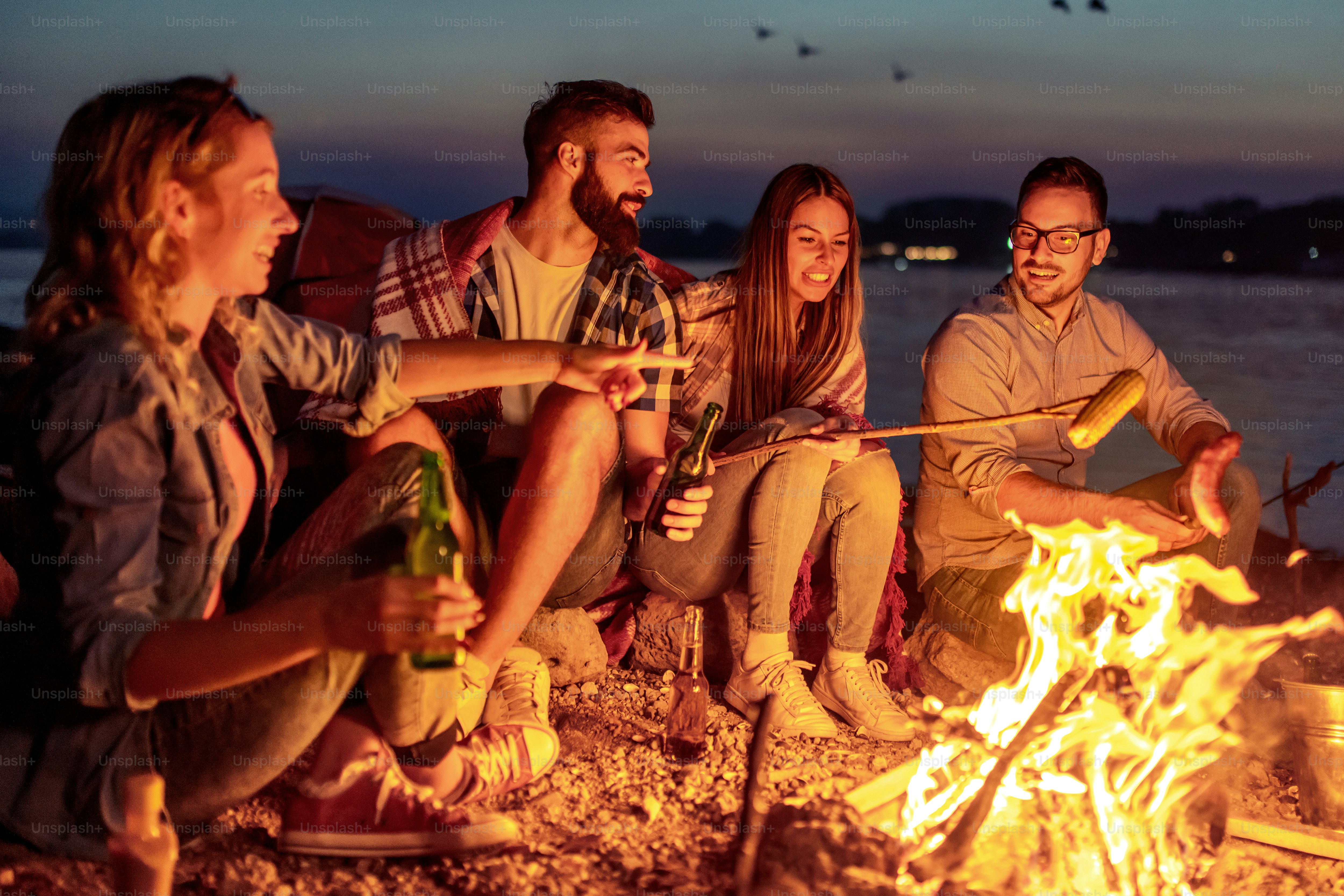 Freunde picknicken am Feuer. Gruppe junger Freunde beim Picknick in der Nacht.
