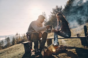 Happy young couple having morning coffee while camping in mountains