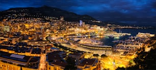 Panorama aereo del porto di Monaco Monte Carlo e dello skyline illuminato della città nel crepuscolo dell'ora blu serale. Vista notturna del porto di Monaco con yacht di lusso