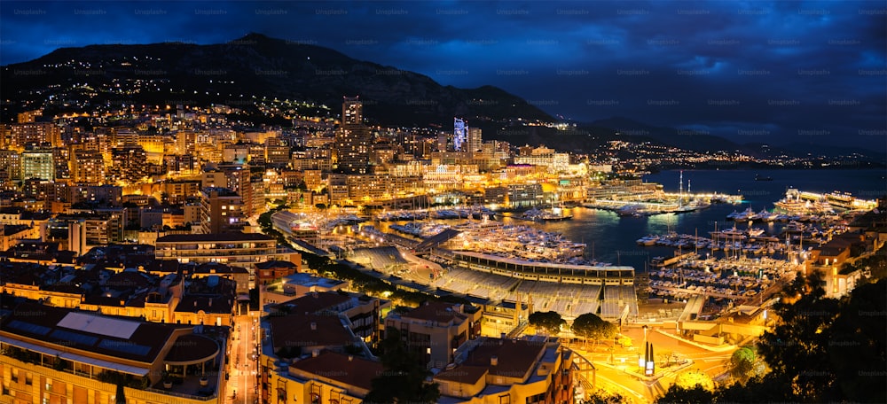 Panorama aéreo del puerto de Montecarlo de Mónaco y el horizonte iluminado de la ciudad en el crepúsculo de la hora azul de la tarde. Vista nocturna del puerto de Mónaco con yates de lujo