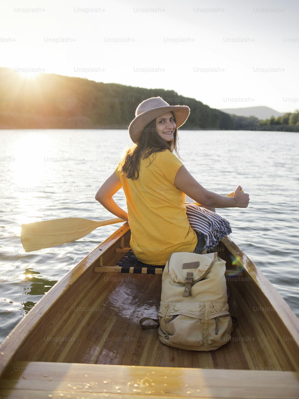 Smiling young woman paddling the canoe on the sunset lake.