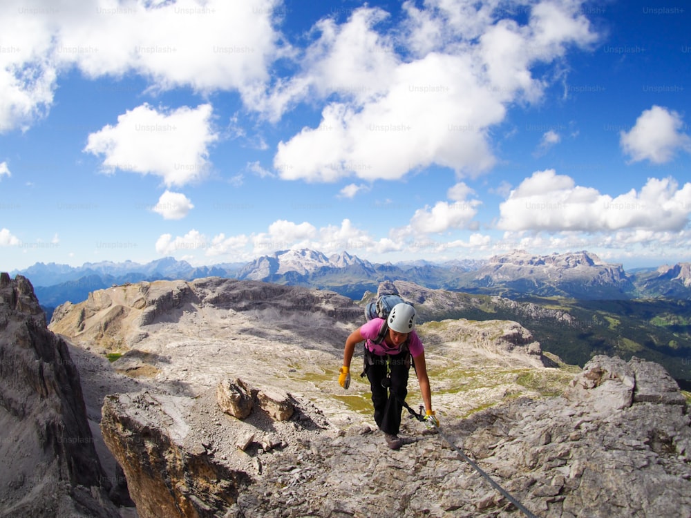 Une alpiniste atteint le sommet avec un grand paysage des Dolomites derrière elle