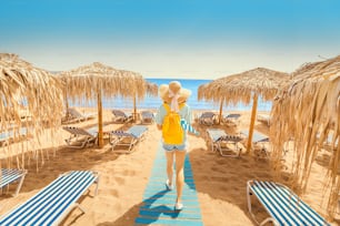 Girl walking on the beach with sunbeds and sun umbrellas. Seaside resort and summer vacation concept