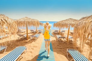 선베드와 태양 우산을 들고 해변을 걷는 소녀. 해변 리조트와 여름 휴가 개념