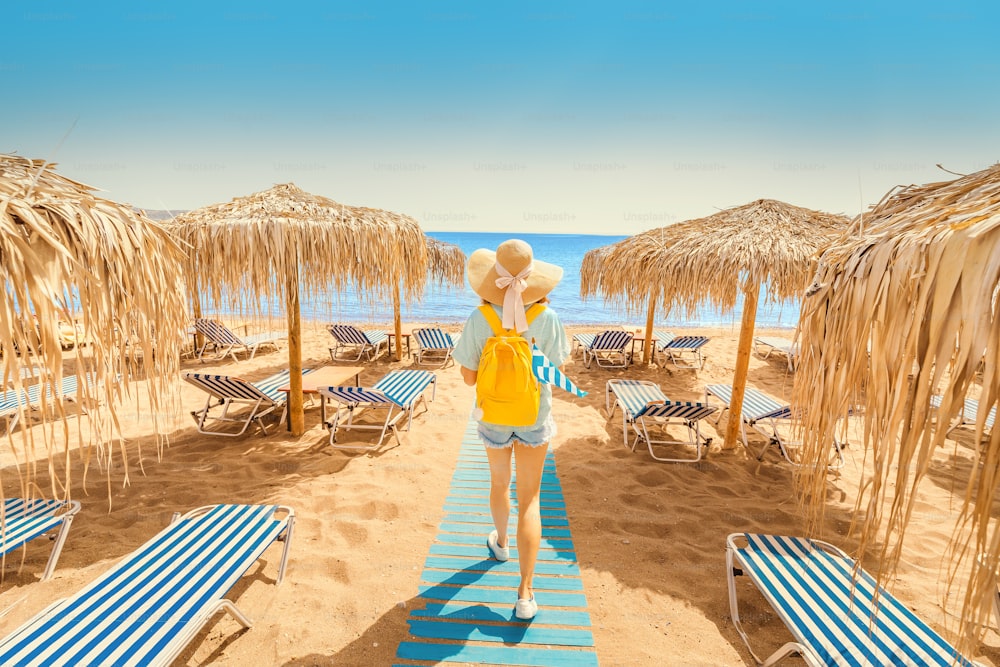 Girl walking on the beach with sunbeds and sun umbrellas. Seaside resort and summer vacation concept