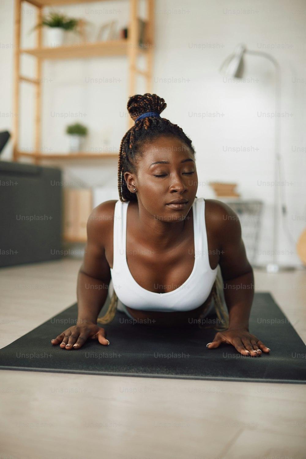 Junge schwarze Sportlerin, die Yoga-Entspannungsübungen praktiziert, während sie zu Hause trainiert.
