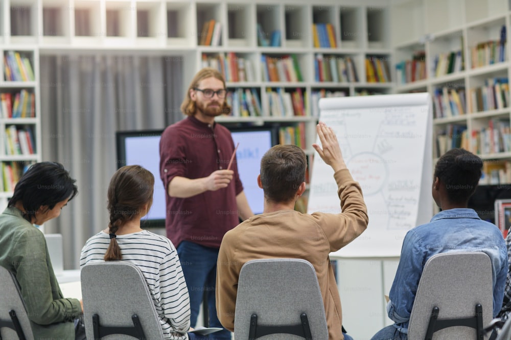 Young businessman standing near the whiteboard and holding the presentation for young people at library