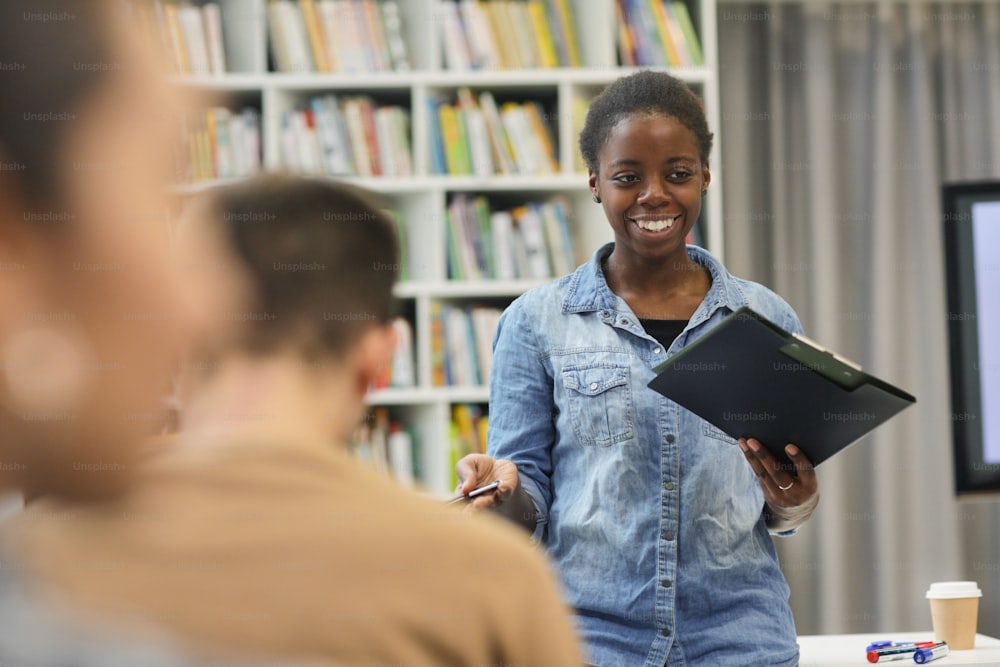 Studente africano sorridente in piedi e che presenta la sua relazione al pubblico in biblioteca