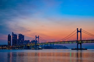 高層ビルとドラマチックな空が広がる日の出の��広安大橋。韓国、釜山