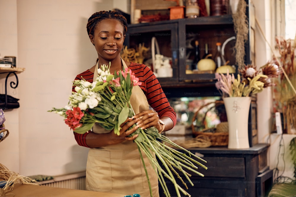 Afroamerikanische Floristin macht einen Strauß frischer Blumen, während sie im Blumenladen arbeitet.