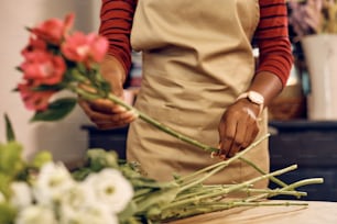 Close up de florista afro-americana organizando flores frescas enquanto trabalha na floricultura.