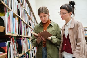 Two young women choosing books for study while standing in the library