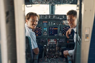 High-spirited attractive middle-aged airline captain and a handsome young pleased first officer sitting in the flight deck