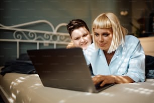 Jovens mulheres gays navegando na internet no laptop enquanto relaxam no quarto.