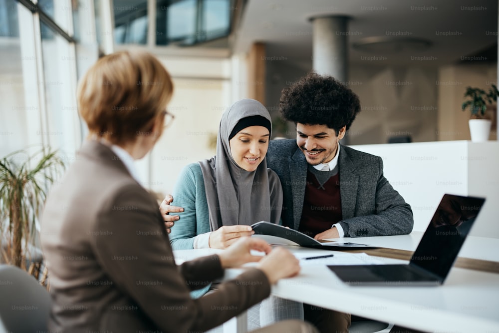 Joven musulmana feliz y su esposo teniendo una reunión con un agente de seguros en la oficina.