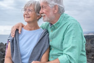 Happy caucasian elderly couple hugging sitting in outdoors at sea. Two senior people enjoying freedom and relax in retirement. Horizon over water