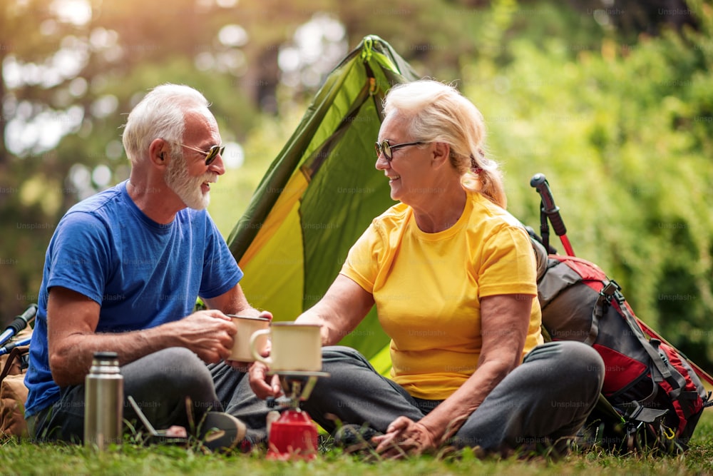 Senior couple enjoying in nature, drinking tea in front of their tent.