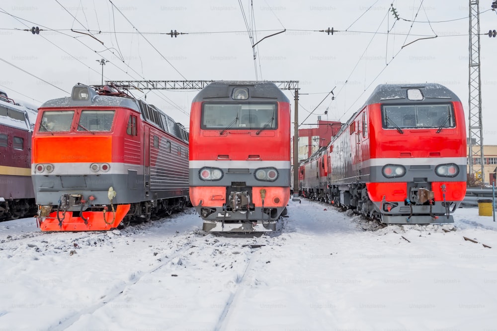 Three red electric locomotives are lined up on the railway in winter snow depot