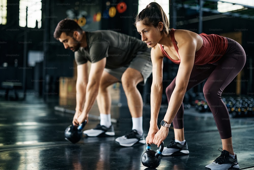 Couple d’athlètes utilisant des kettlebells lors d’un entraînement croisé dans un gymnase.