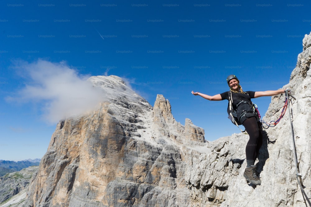 attractive blonde female mountain climber on a steep Via Ferrata in the South Tyrol waving and smiling