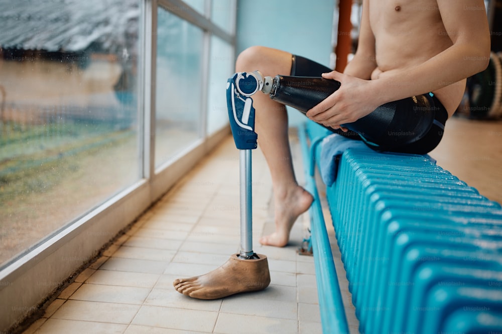 Nadador irreconhecível com deficiência ajustando sua perna artificial após o treinamento esportivo.