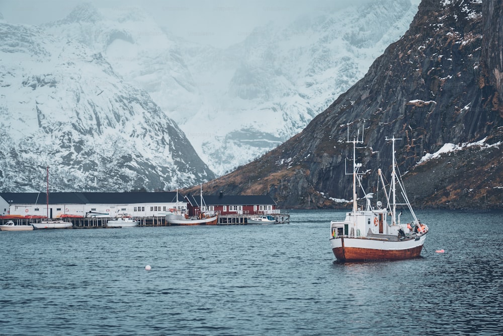 Ship fishing boat in Hamnoy fishing village on Lofoten Islands, Norway with red rorbu houses. With falling snow