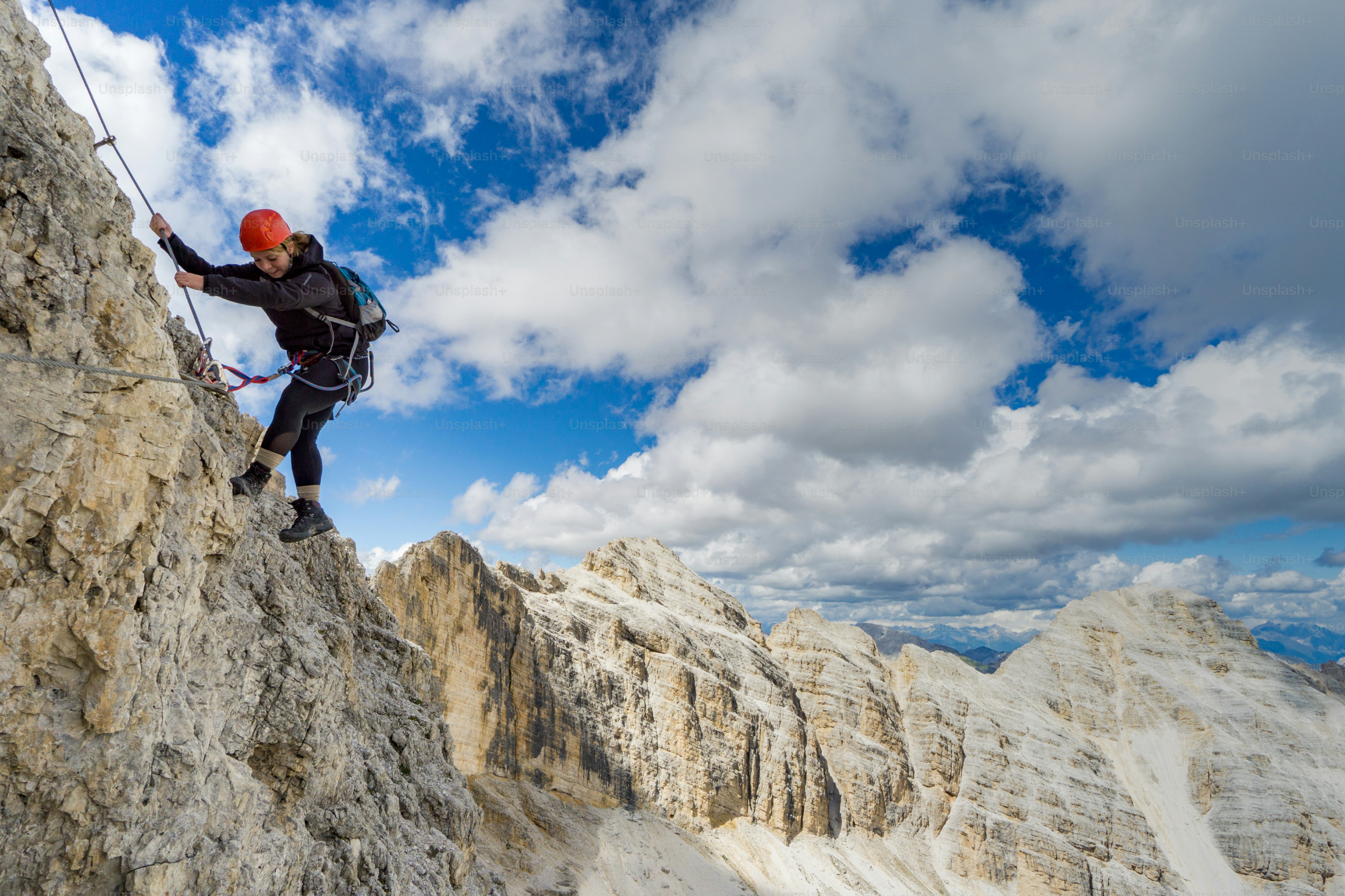 Pemandangan horizontal pendaki gunung wanita di Via Ferrata yang curam di Dolomites Italia dengan pemandangan indah di belakang