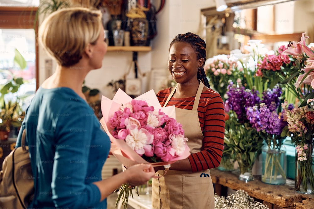 幸せなアフリカ系アメリカ人の花屋の店員が、顧客に新鮮な花束を贈っています。