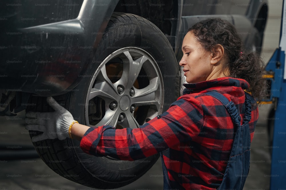 Technicienne automobile en gants de travail changeant la roue d’une automobile dans une station-service de réparation