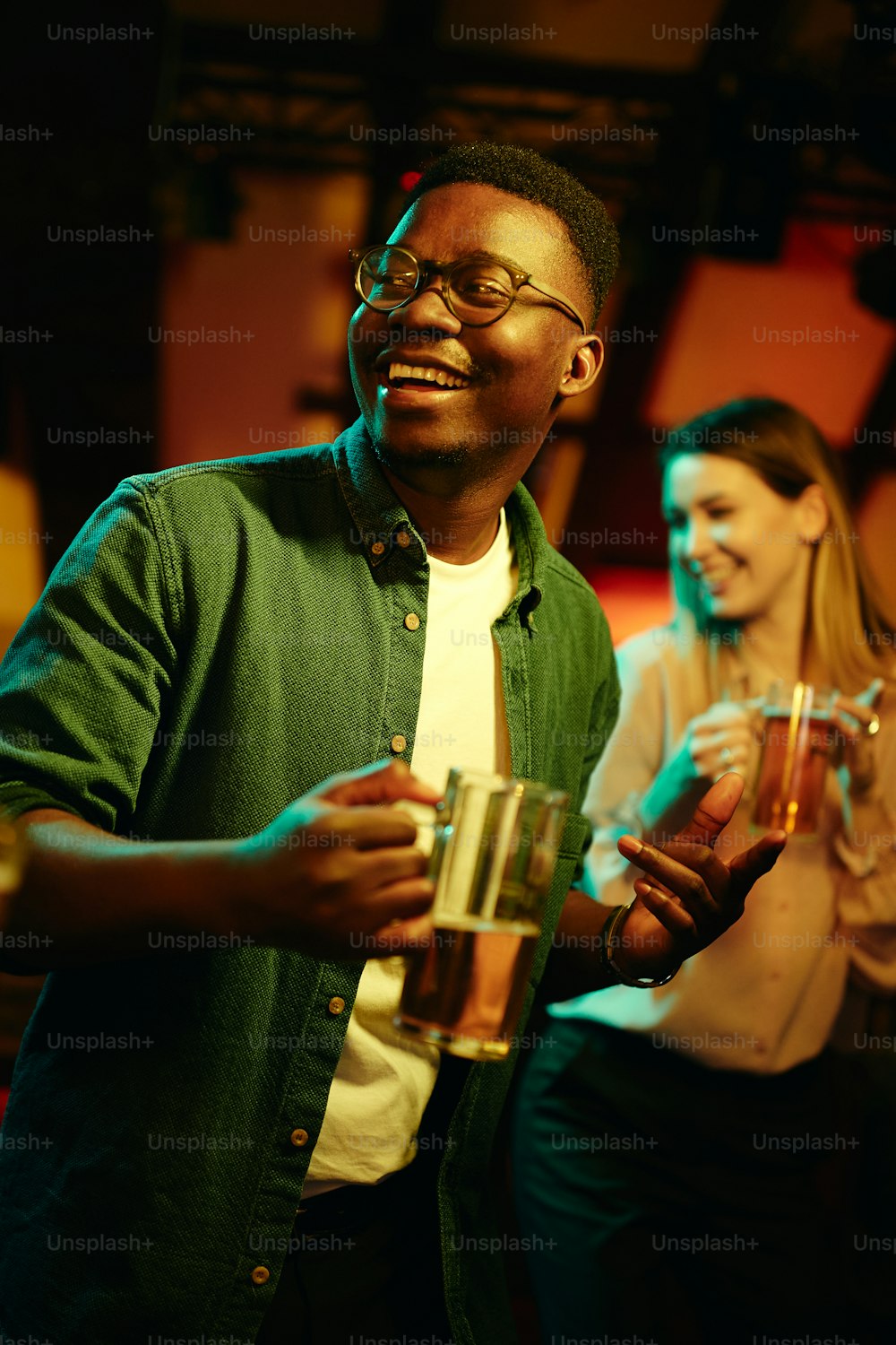 Uomo nero felice che beve birra e balla durante la notte in un bar.