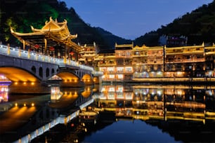 Chinese tourist attraction destination - Feng Huang Ancient Town (Phoenix Ancient Town) on Tuo Jiang River with bridge illuminated at night. Hunan Province, China